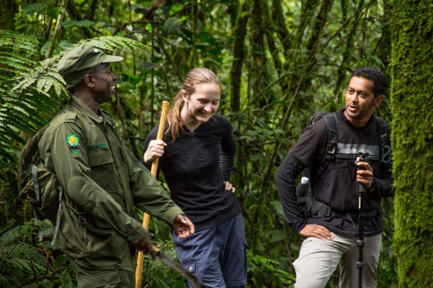 Uganda Wildlife Authority ranger briefing two tourists with walking sticks in a lush, mossy rainforest