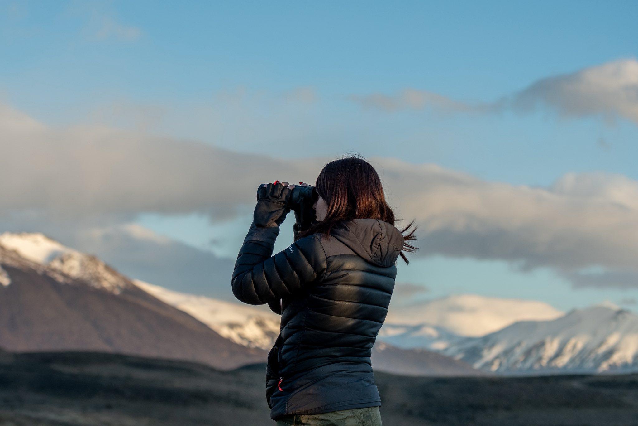 Woman using binoculars to scan Patagonia landscape during puma tracking